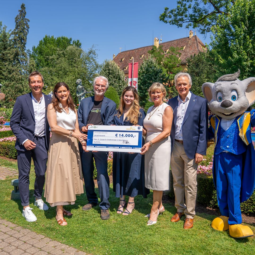 Gruppenfoto bei der SpendenĂŒbergabe im Park â Vertreter:innen mit einem Scheck ĂŒber 14.000 Euro, begleitet vom LEONARDO Maskottchen.