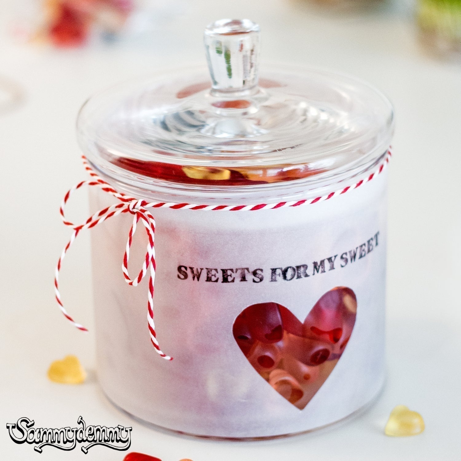 Glasdose mit Deckel, gefüllt mit roten Gummibärchen, dekoriert mit weißem Transparentpapier, Herz-Ausschnitt und dem gestempelten Schriftzug „SWEETS FOR MY SWEET“, verziert mit rot-weißem Band.
