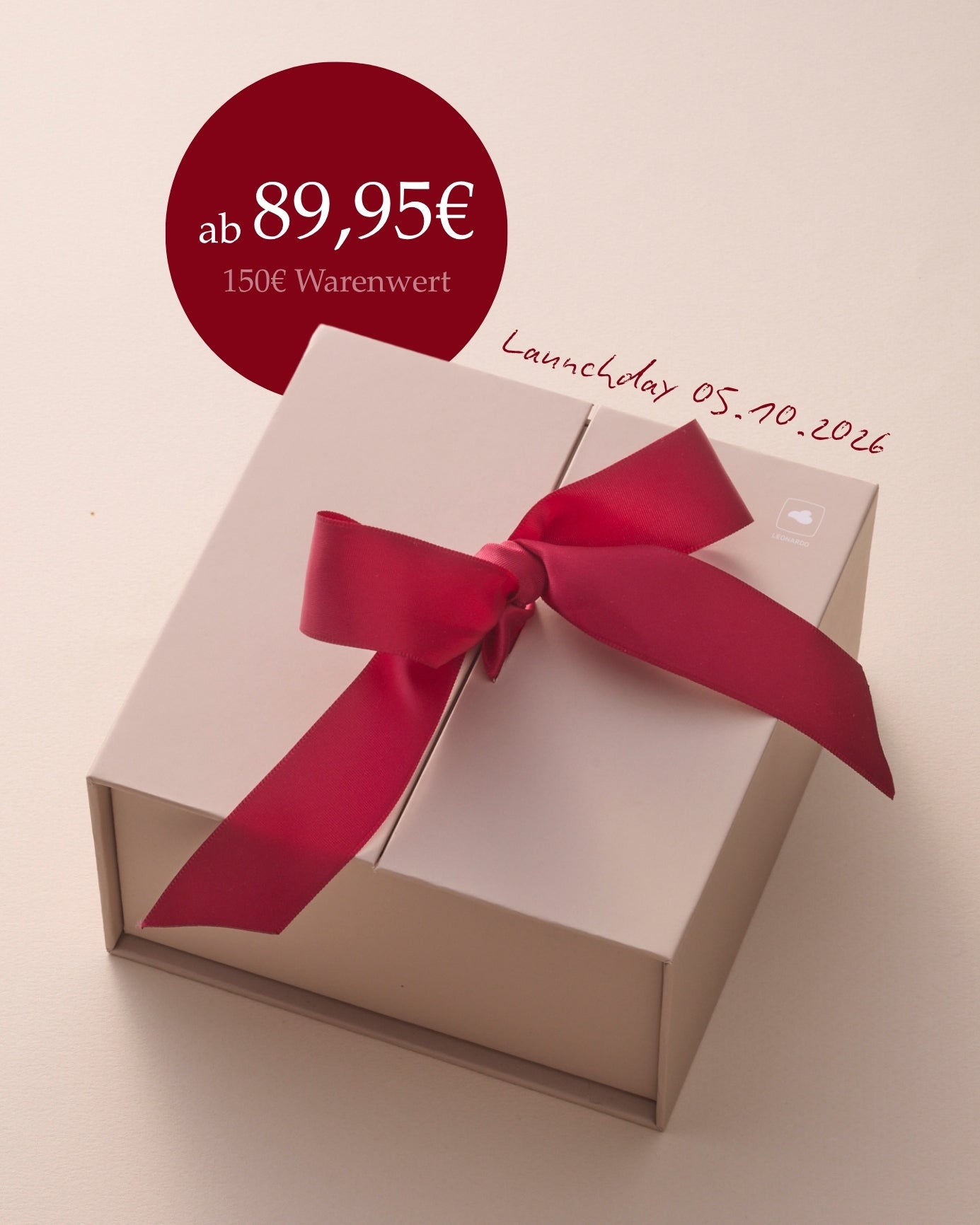 ab 89,95€, 150€ Warenwert, Launchday 05.10.2026, cremefarbene Geschenkbox mit roter Schleife auf beigem Hintergrund