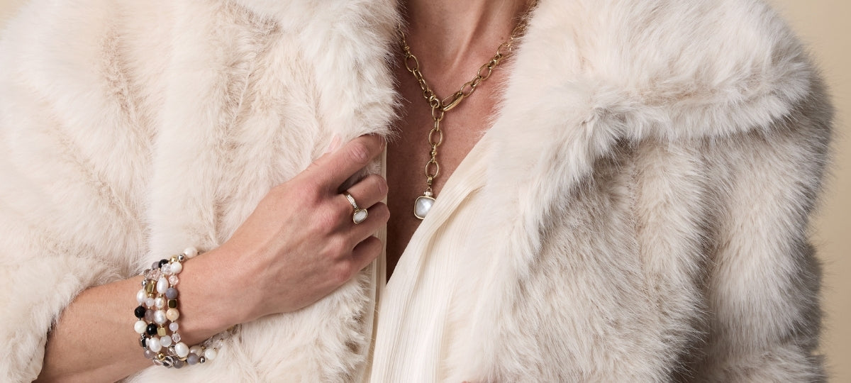 Frau trägt eleganten weißen Pelzmantel mit Perlenkette, Armband und Ring in silberner Optik
