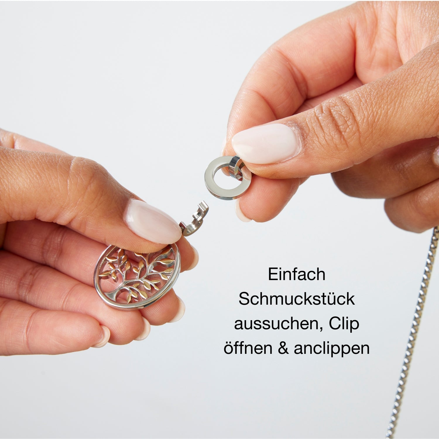 Zwei Hände zeigen, wie ein runder Clip-Verschluss geöffnet und ein Anhänger mit filigranem Lebensbaum eingeklippt wird. Daneben steht: „Einfach Schmuckstück aussuchen, Clip öffnen & anclippen“.