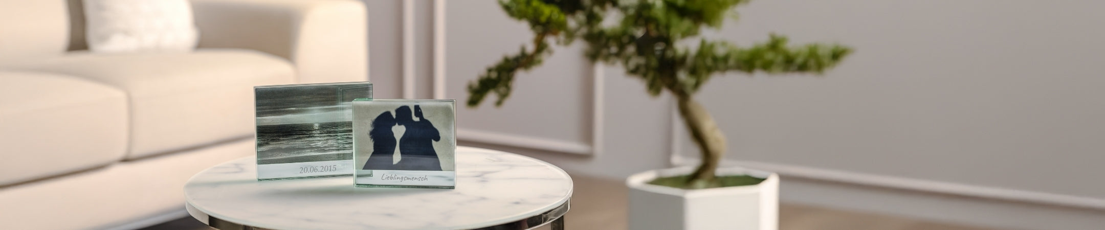 Moderne Wohnzimmerszene mit personalisierten Fotoblöcken auf Marmortisch, Bonsai und heller Couch im Hintergrund