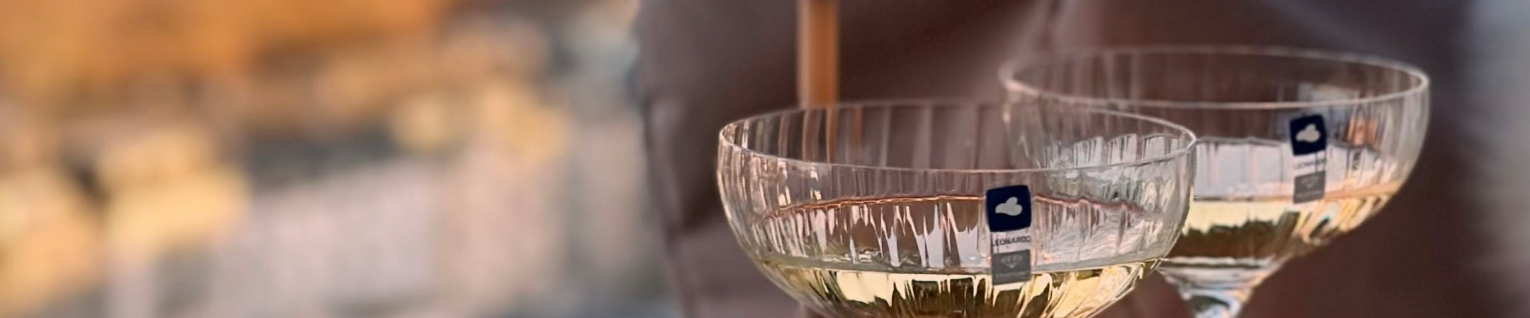 Zwei Champagnergläser mit Weißwein vor unscharfem Hintergrund in warmer Lichtatmosphäre