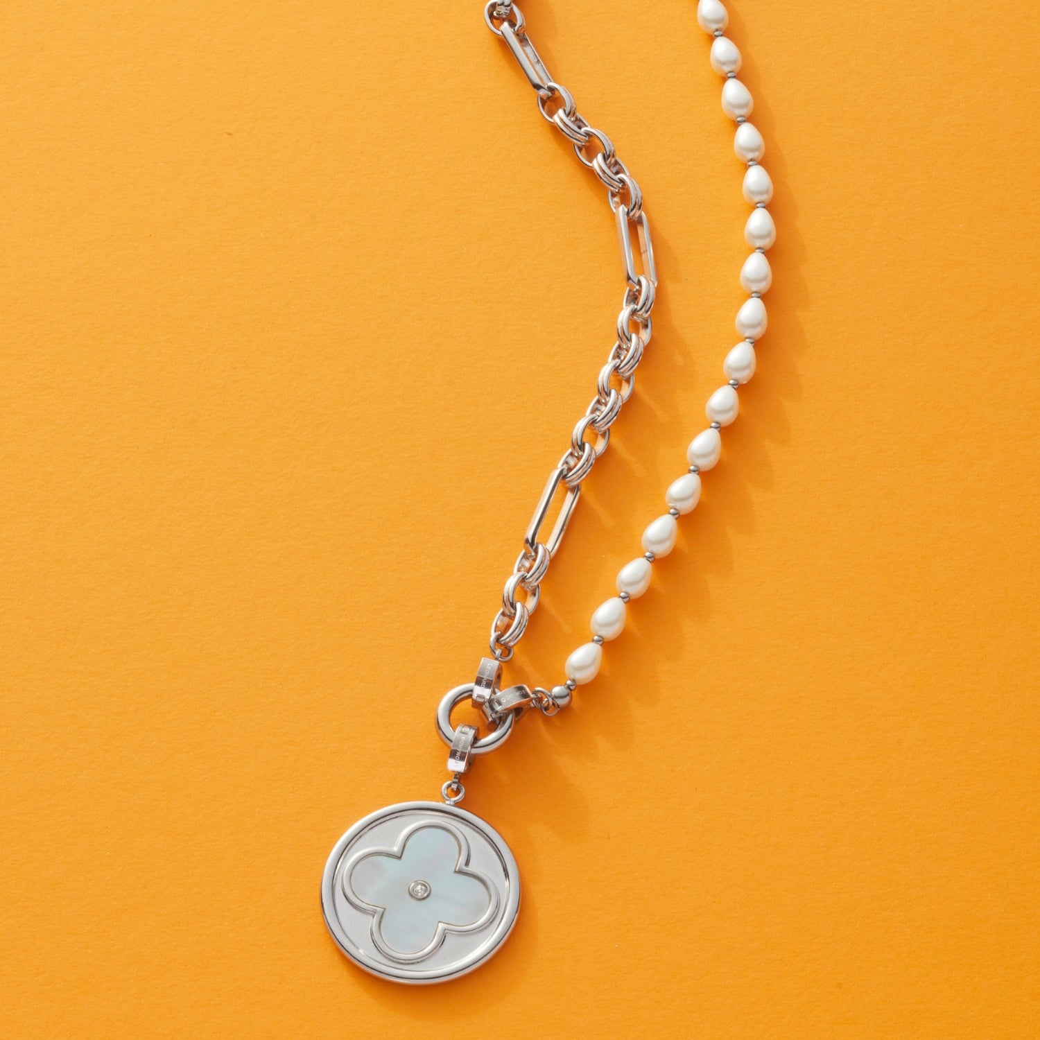 Silberne Halskette mit Perlenstring und Gliederkette, vier-blättriger Blumenanhänger, orangefarbener Hintergrund