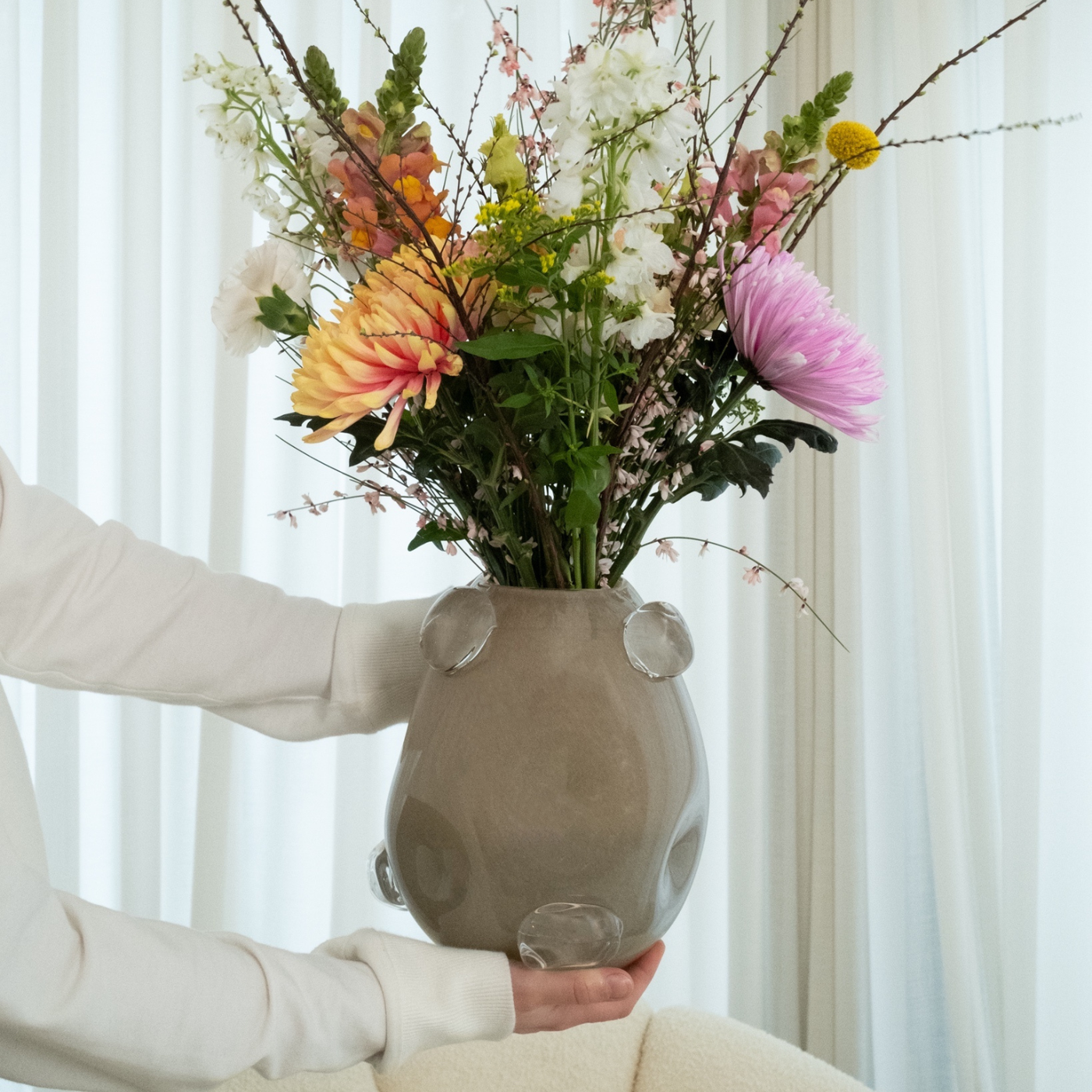 Große beige Glasvase mit runden Glaselementen, gefüllt mit einem bunten Blumenstrauß.