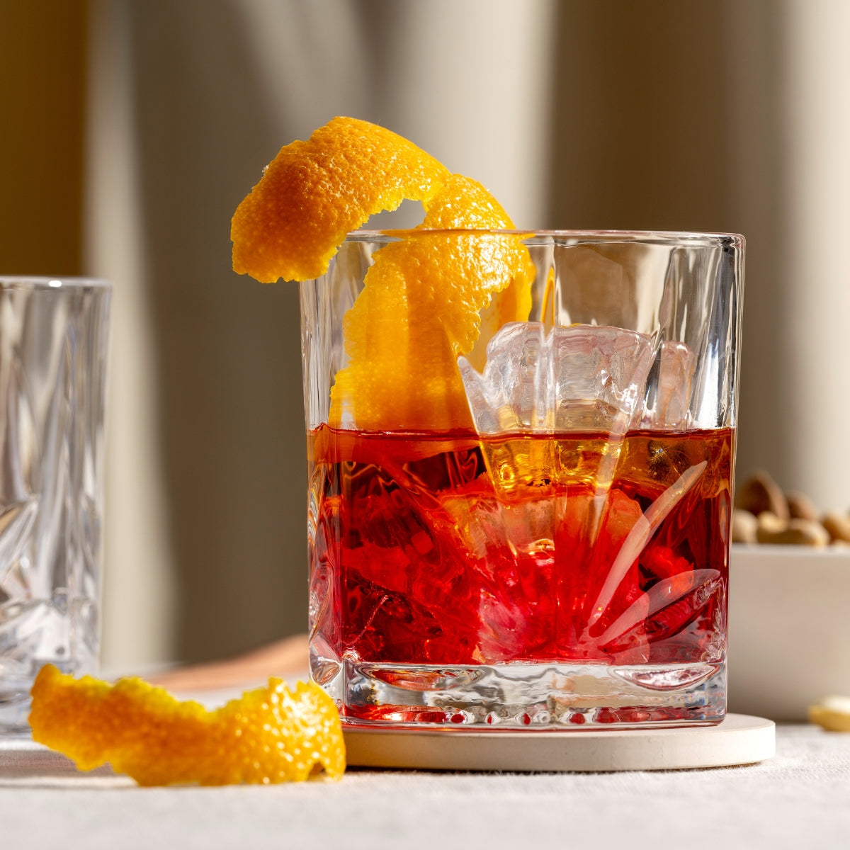 Der markante Tumbler mit tiefem Schliff wird zum Blickfang auf dem gedeckten Tisch – gefüllt mit einem klassischen Negroni und veredelt mit einer dekorativen Orangenzeste.