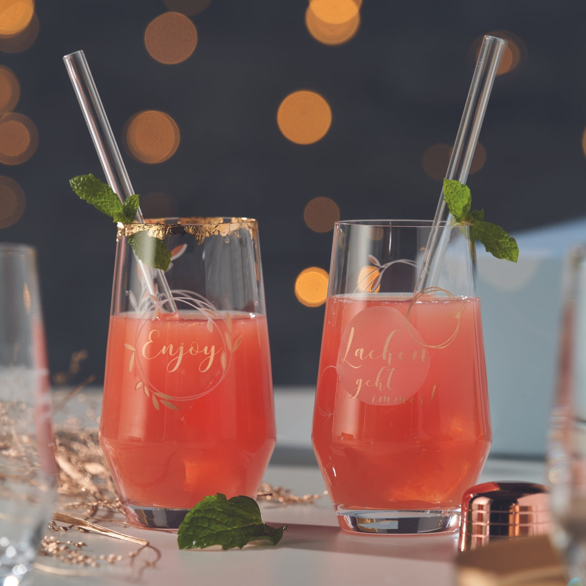 Zwei Gläser mit Fruchtcocktails und Glasstrohhalmen, verziert mit Schriftzug und Goldrand.