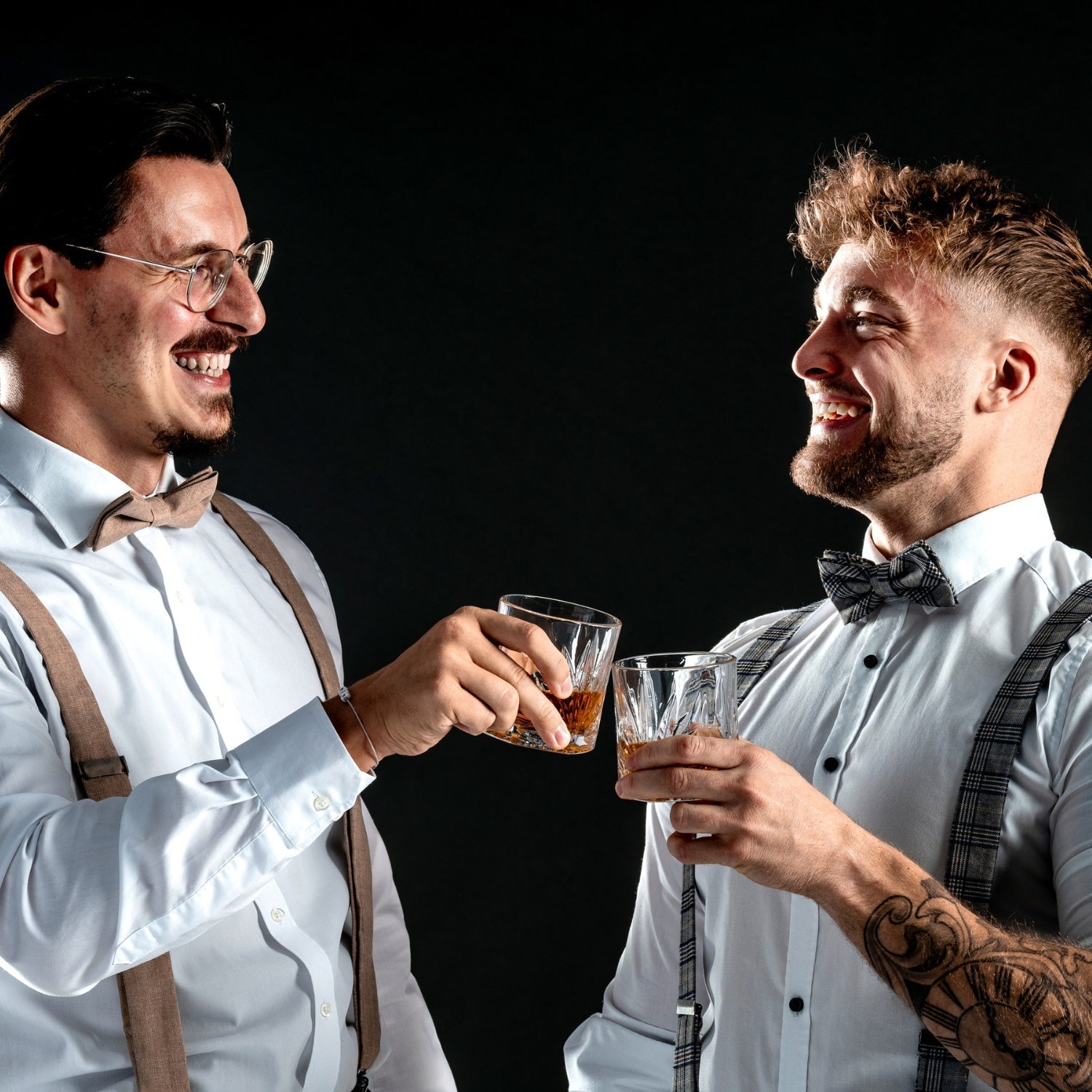 Zwei festlich gekleidete Männer lachen und stoßen mit eleganten LEONARDO Whiskeygläsern vor dunklem Hintergrund an.