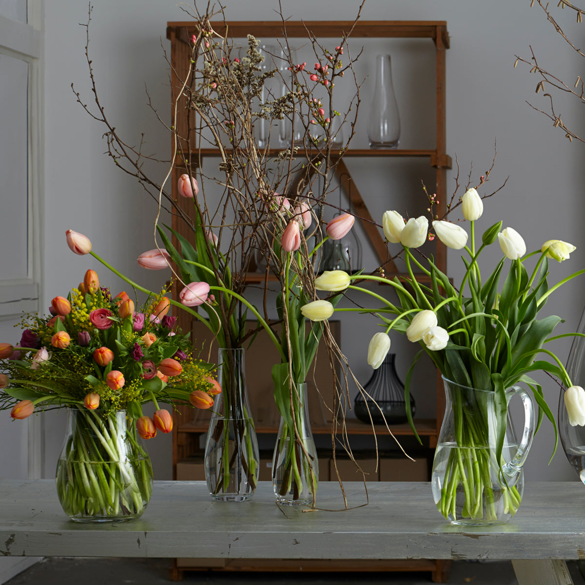 Drei klare Glasvasen mit Tulpen und Zweigen auf grauem Tablett