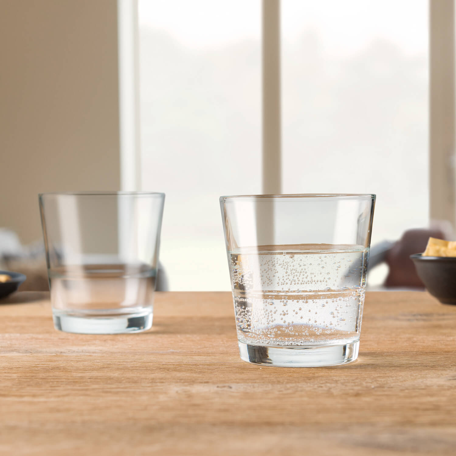 Zwei Trinkgläser EVENT auf Holztisch, eines leer, eines mit Wasser gefüllt