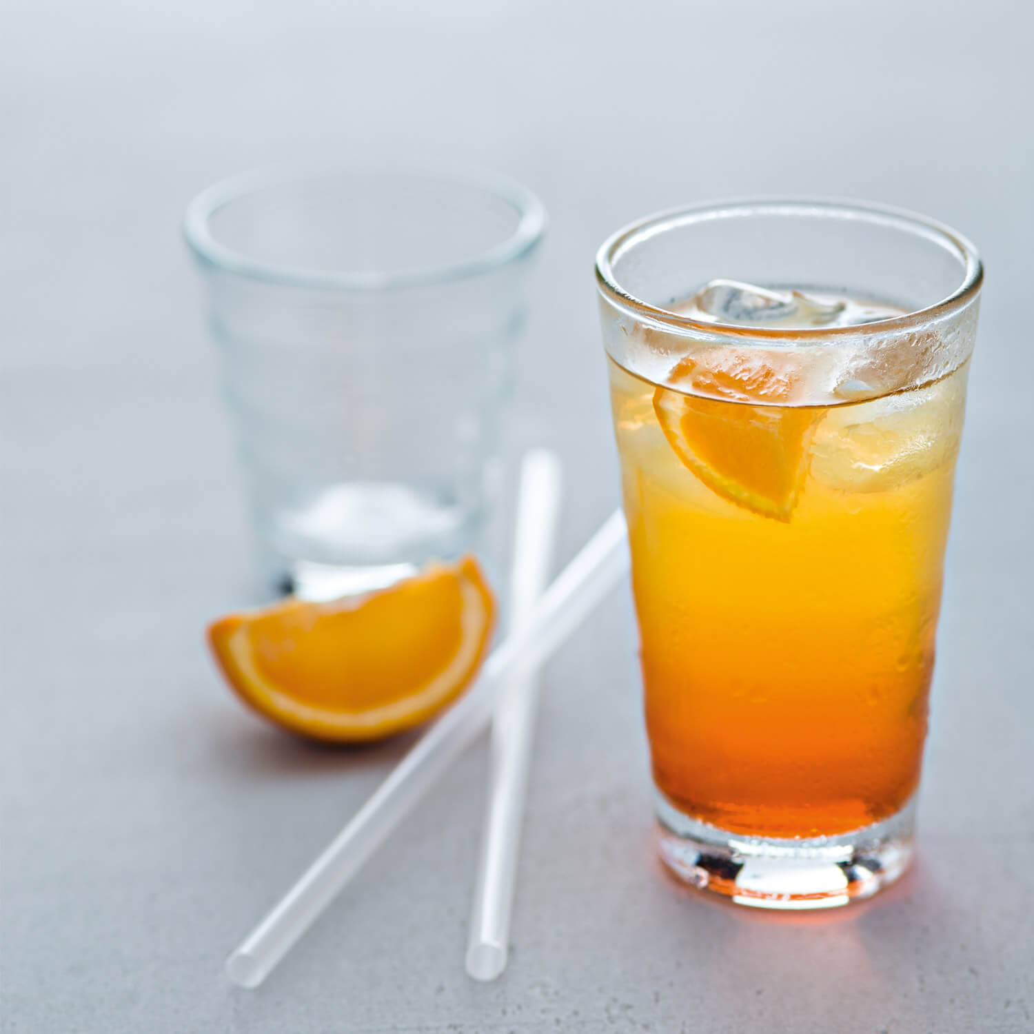 Klare Gläser mit Orangensaft und Eiswürfeln, Orangenscheibe und Strohhalme