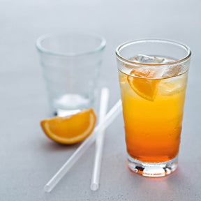Klare Gläser mit Orangensaft und Eiswürfeln, Orangenscheibe und Strohhalme