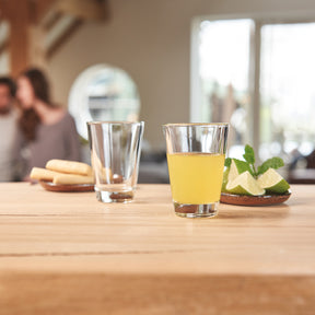Stamper CIAO auf Holztisch in Kueche, einer mit Wasser gefuellt, einer mit gelbem Getraenk und Minze