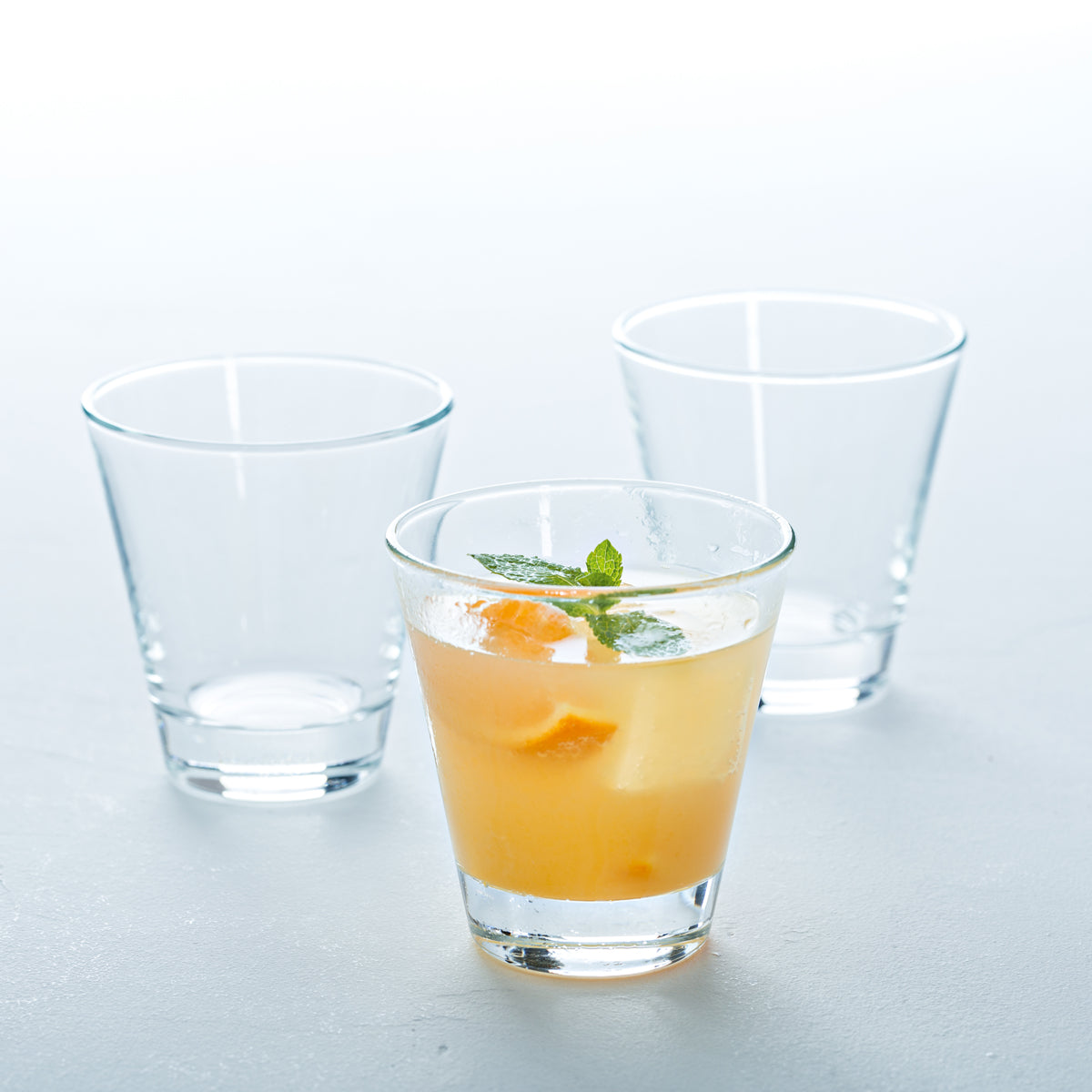 Trinkglas CIAO mit Orangensaft und Minze, zwei leere Gläser daneben