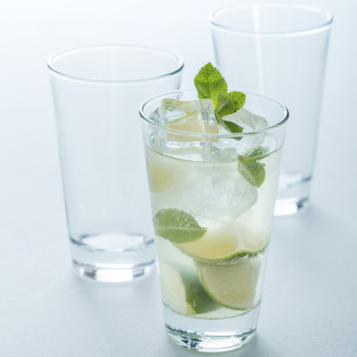 Trinkglas CIAO mit Limone, Minze und Eiswürfeln gefüllt, daneben zwei leere Gläser