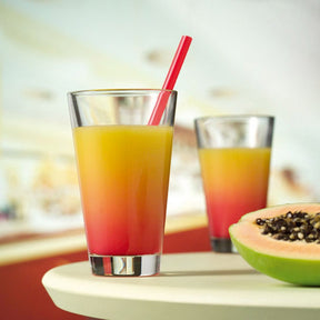 Trinkglas CIAO mit Saft gefüllt, daneben halbe Papaya, zweites Glas im Hintergrund