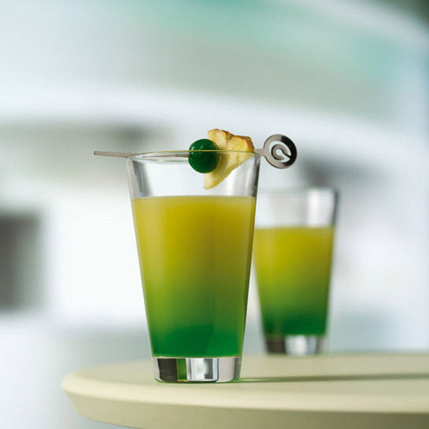 Trinkglas CIAO mit grünem und gelbem Cocktail, Olivengarnitur und Rührstab auf hellem Tisch
