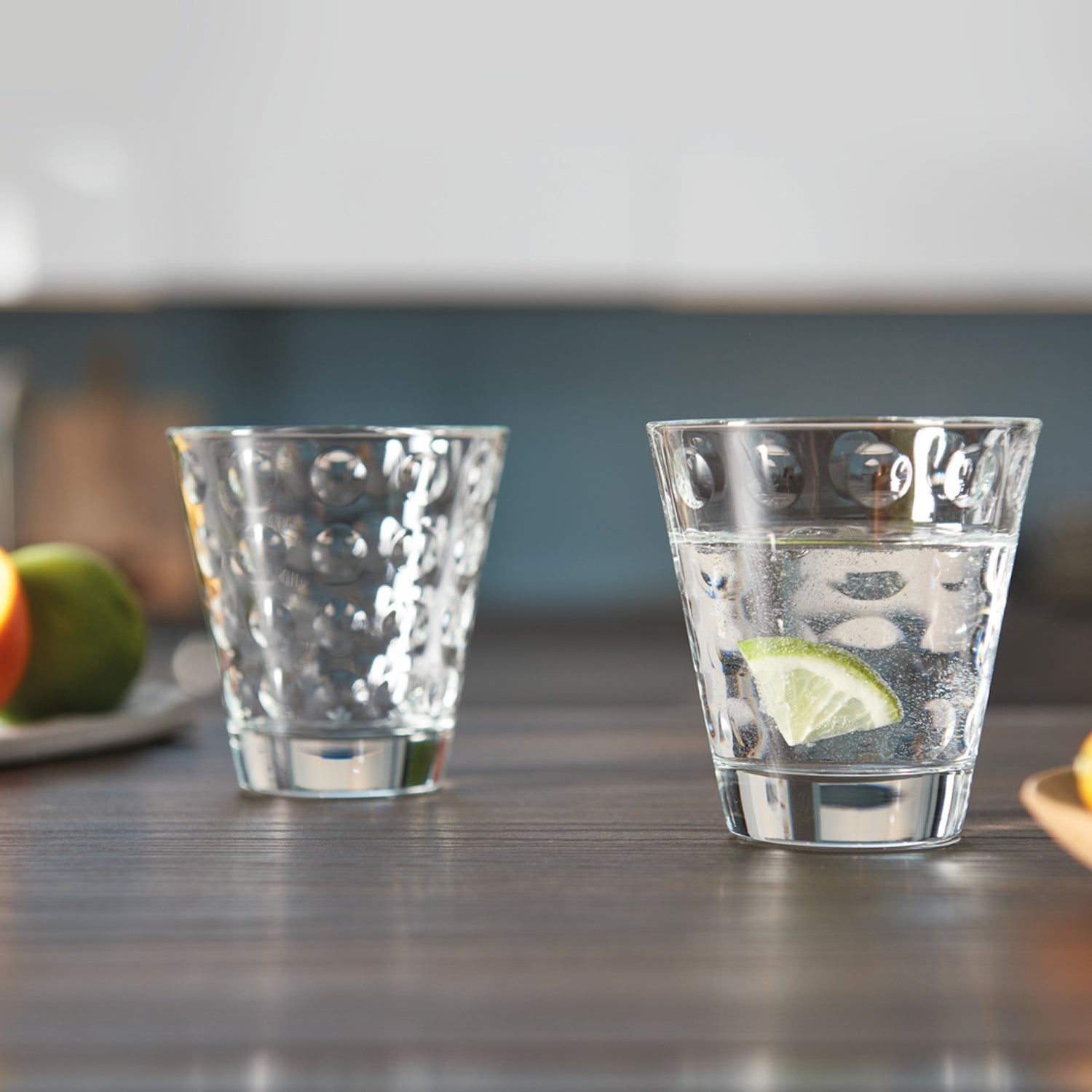 Zwei Trinkgläser OPTIC auf Küchentheke, eines mit Wasser und Limettenscheibe, eines mit Mineralwasser