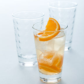 Trinkglas OPTIC mit Orangenscheibe und Eiswürfeln, zwei leere Gläser im Hintergrund