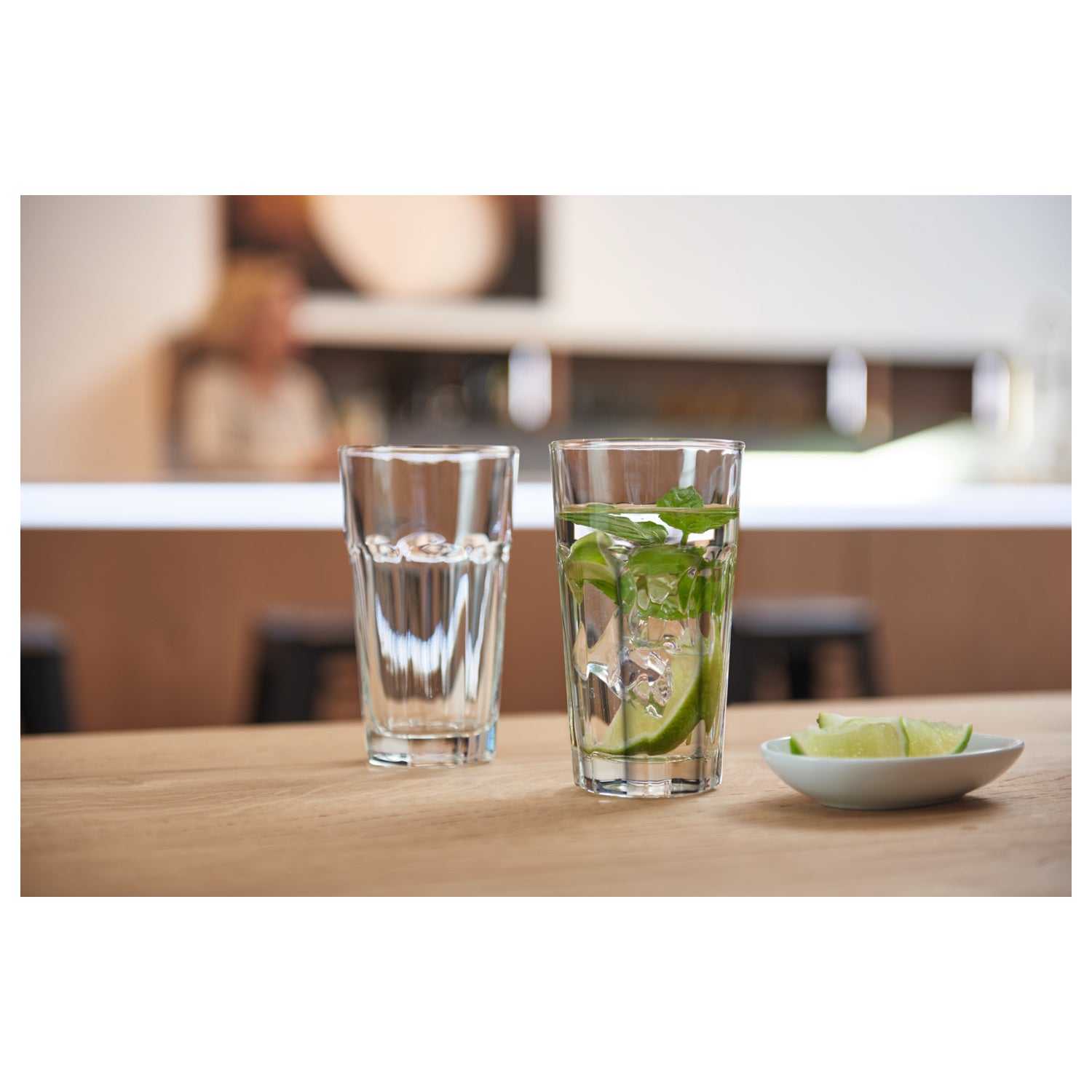 Longdrinkglas ROCK auf Holztisch, eines mit Wasser gefüllt, eines mit Mojito, daneben Limettenscheiben