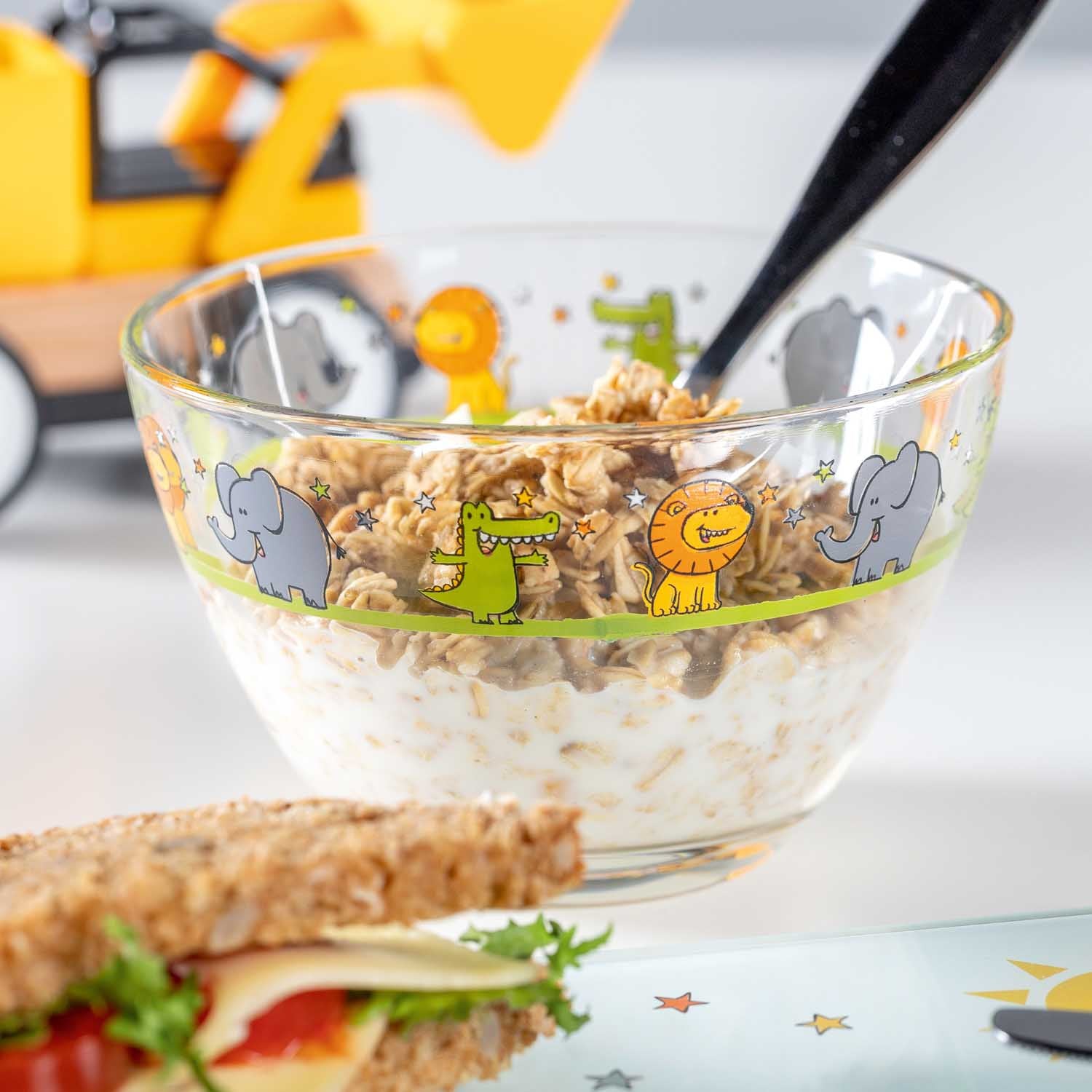 Schale BAMBINI gefüllt mit Müsli und Milch, daneben belegtes Brötchen, Frühstückstisch