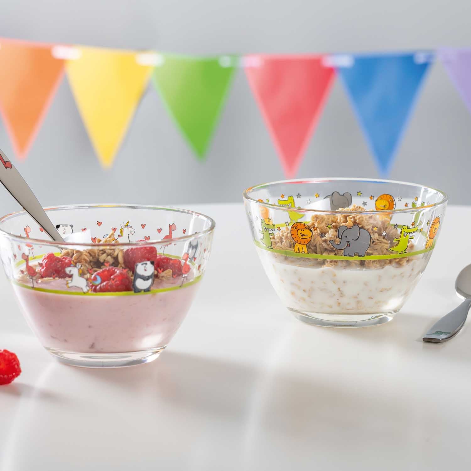 Zwei Glasschalen BAMBINI mit Müsli und Joghurt, bunte Wimpelgirlande im Hintergrund