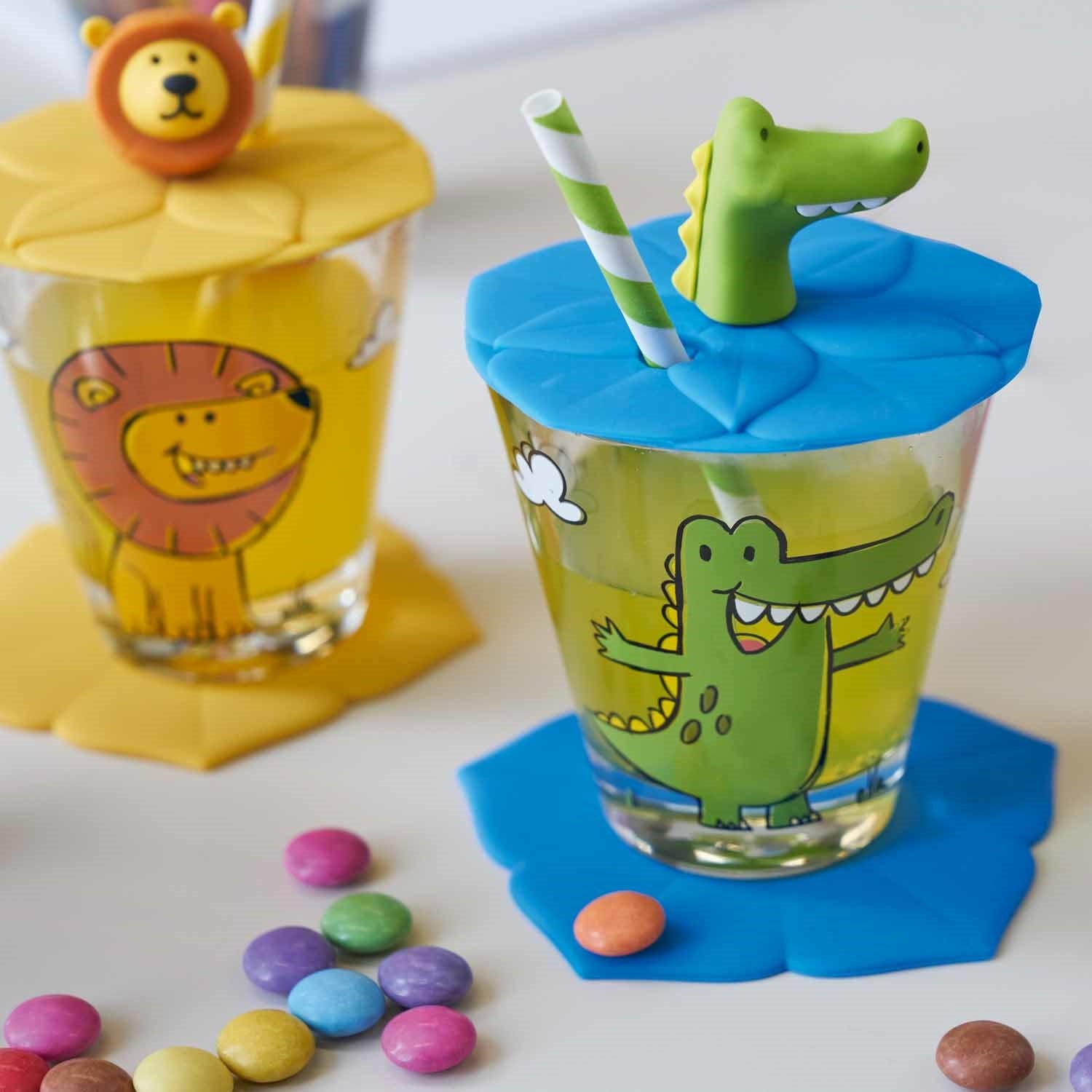 Trinkglas BAMBINI mit Krokodil-Motiv, blauem Deckel und Strohhalm, daneben Löwe-Becher, bunte Bonbons