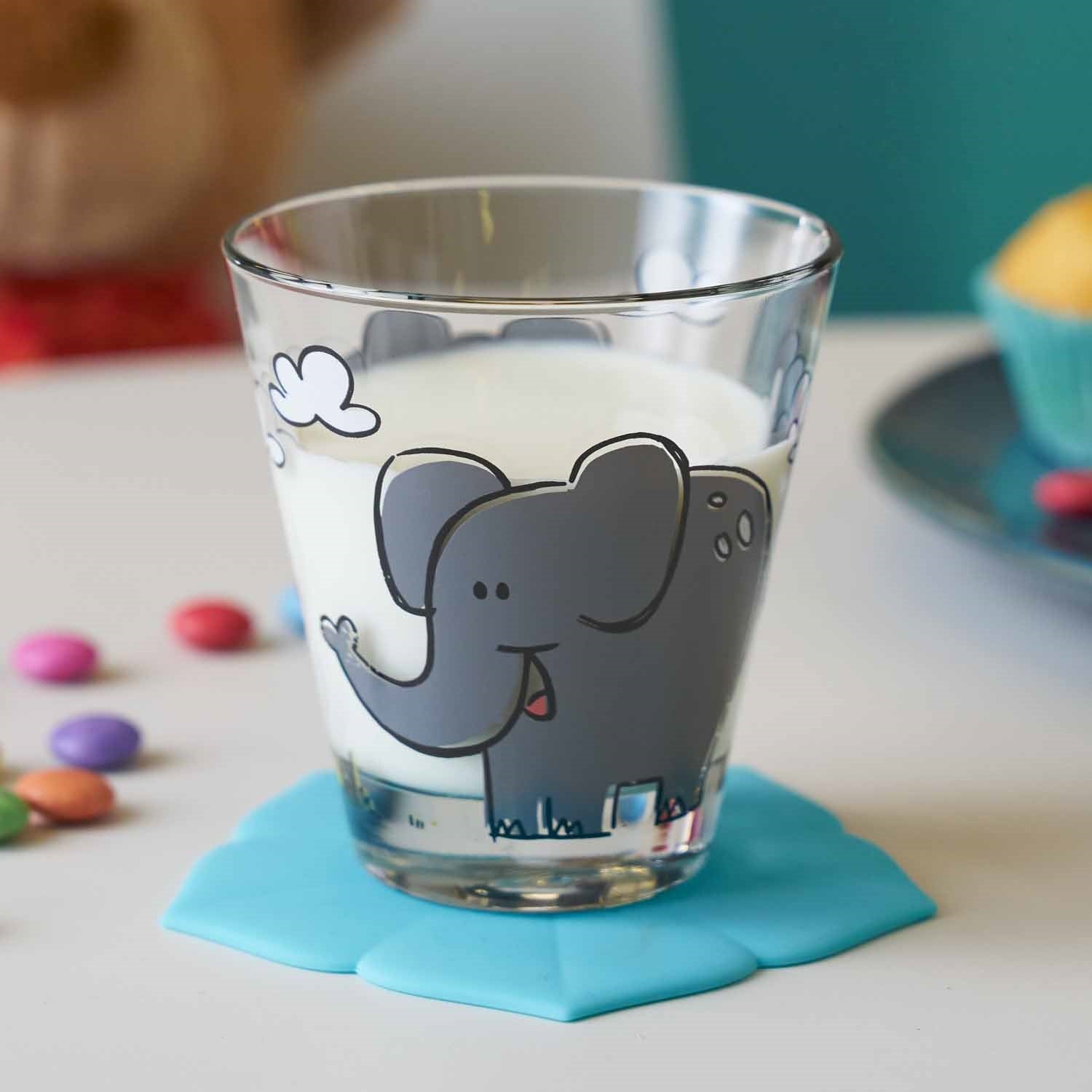 Trinkglas BAMBINI mit Elefantenmotiv auf blauem Untersetzer, bunte Perlen daneben