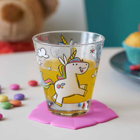 Kinderbecher BAMBINI mit gelbem Einhorn-Motiv, rosa Untersetzer, bunte Perlen und Teddy im Hintergrund