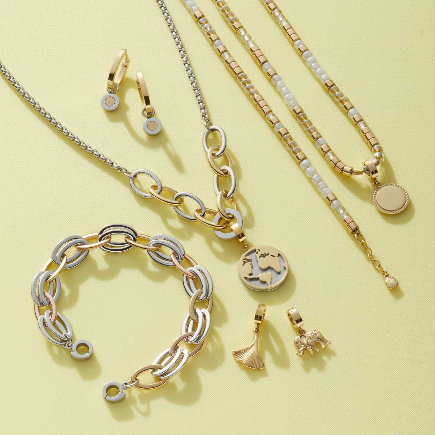 Goldene Creole RONIA Beauty's mit Kettenhalsketten, Armband und Charms auf gelblichem Hintergrund