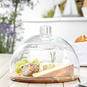 Glasglocke CUCINA mit Holzplatte, Käse, Trauben und Rosmarin auf gedecktem Tisch