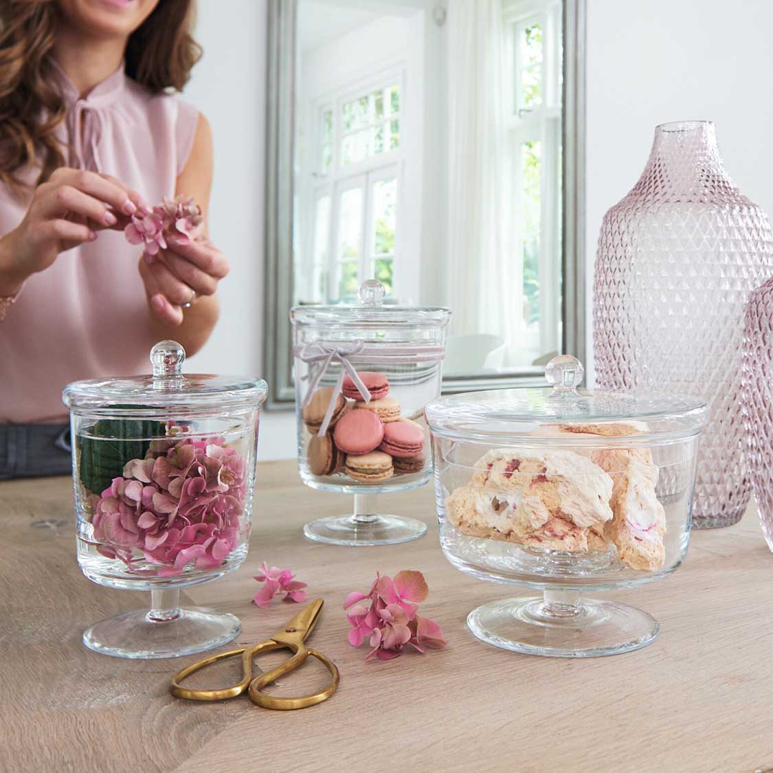 Dose auf Fuß POESIA mit Blüten und Macarons auf Tisch, Frau arrangiert Dekoration