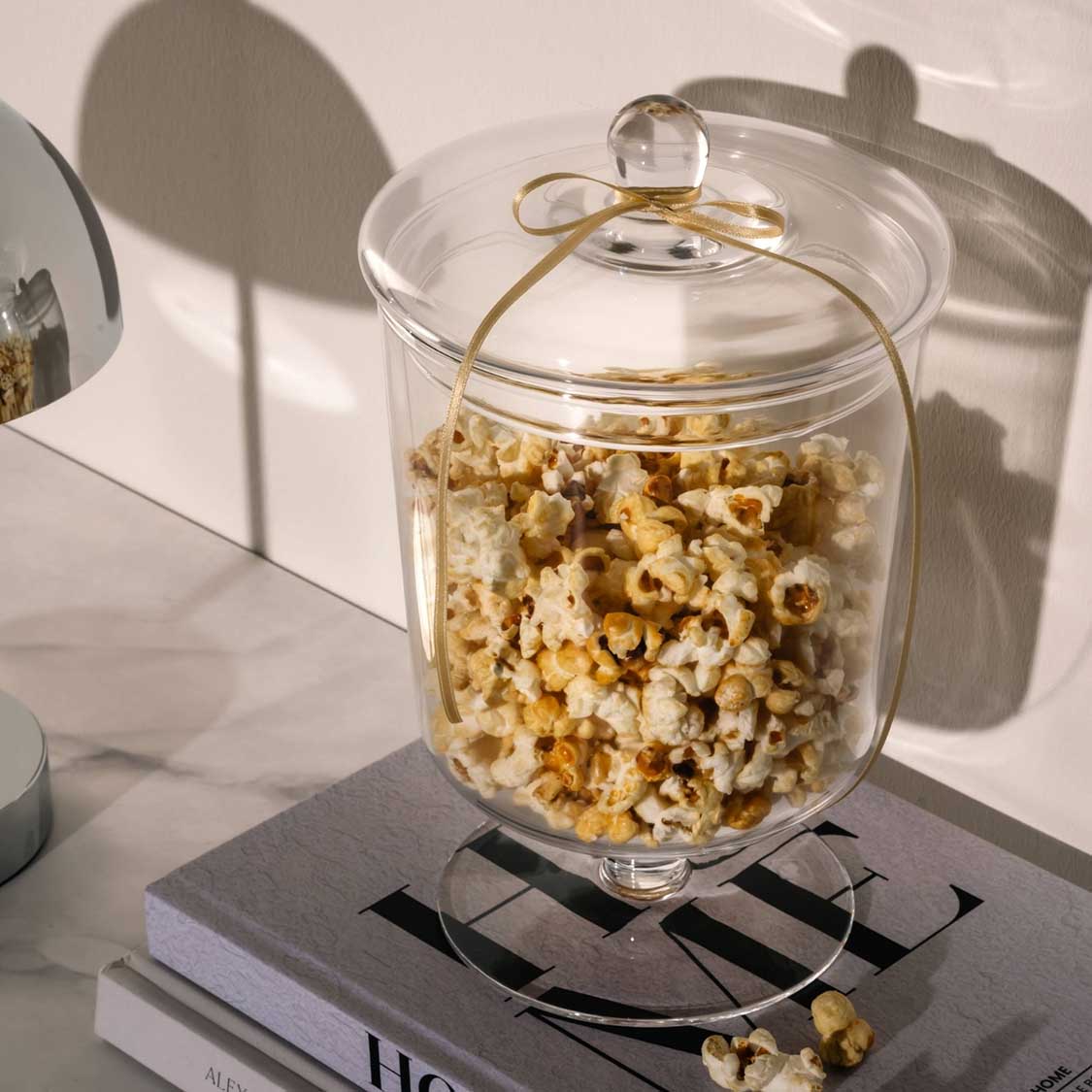 Glaskose POESIA mit Popcorn gefüllt auf Fuß, Sonnenlicht wirft Schatten