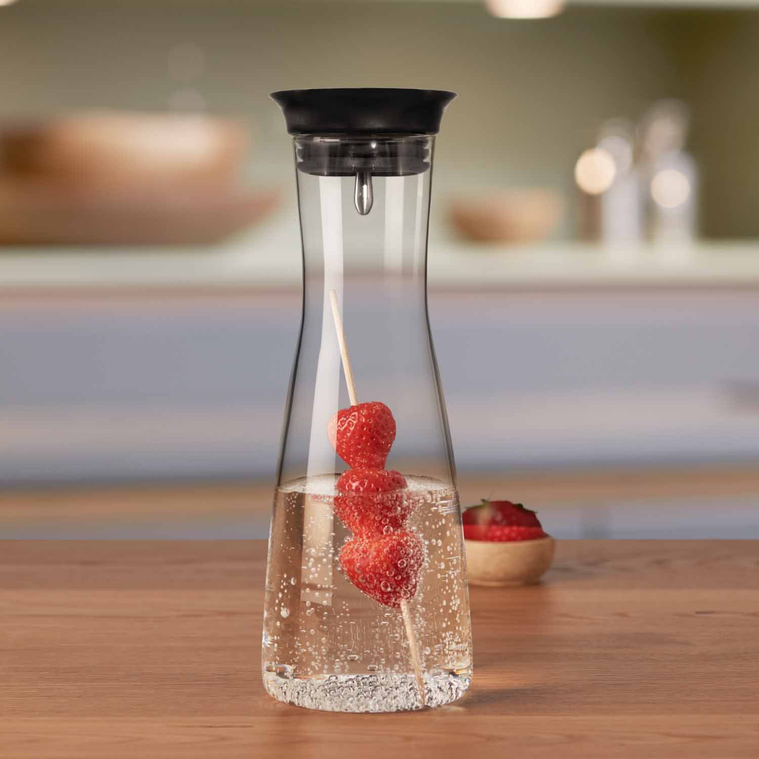 Wasserkaraffe CIAO mit Himbeeren in Wasser auf Holztisch in Küche