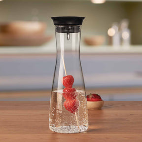Wasserkaraffe CIAO mit Himbeeren in Wasser auf Holztisch in Küche