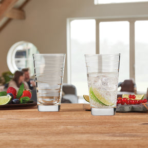 Trinkglas VARIO 280 ml mit Wasser und Limette, daneben leeres Glas, Früchte auf Holztisch, helles Wohnzimmer