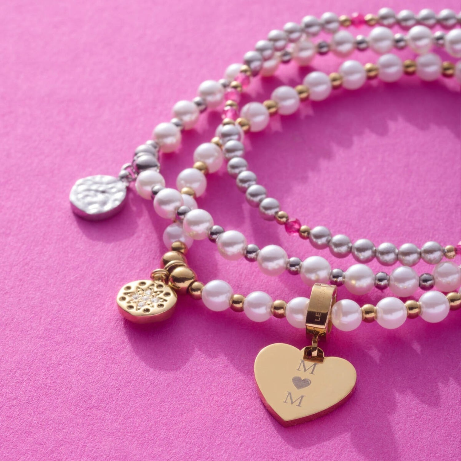 Anhänger JANA gold mit Gravur auf Perlenketten vor rosa Hintergrund