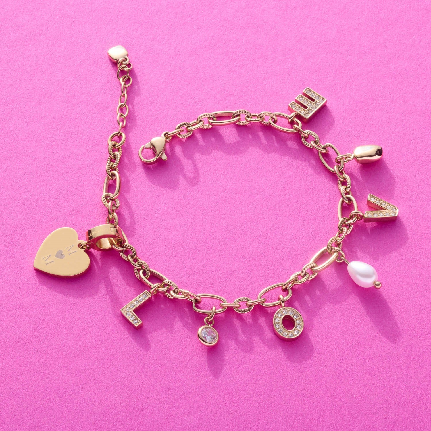 Charm-Armband JANA gold mit verschiedenen Anhängern auf rosa Hintergrund