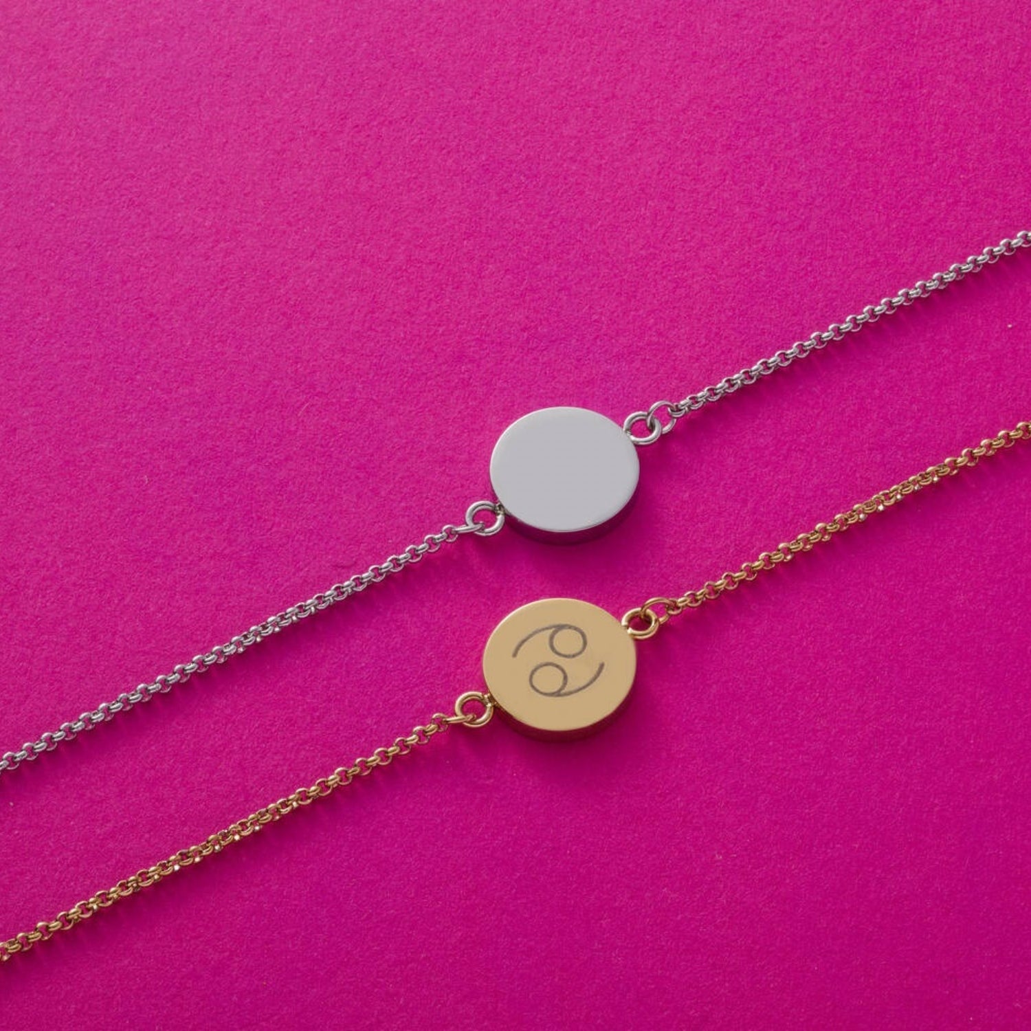Zwei Armbänder mit Plaketten auf pink Hintergrund, eine Plakette silbern, eine gold mit Gravur