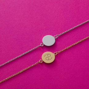 Zwei Armbänder mit Plaketten auf pink Hintergrund, eine Plakette silbern, eine gold mit Gravur