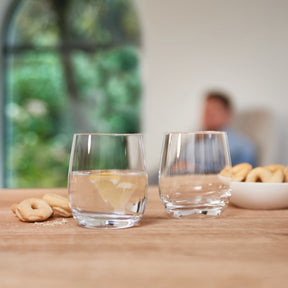Trinkglas TIVOLI mit Wasser und Zitrone, Gebäck auf Holztisch, Person im Hintergrund