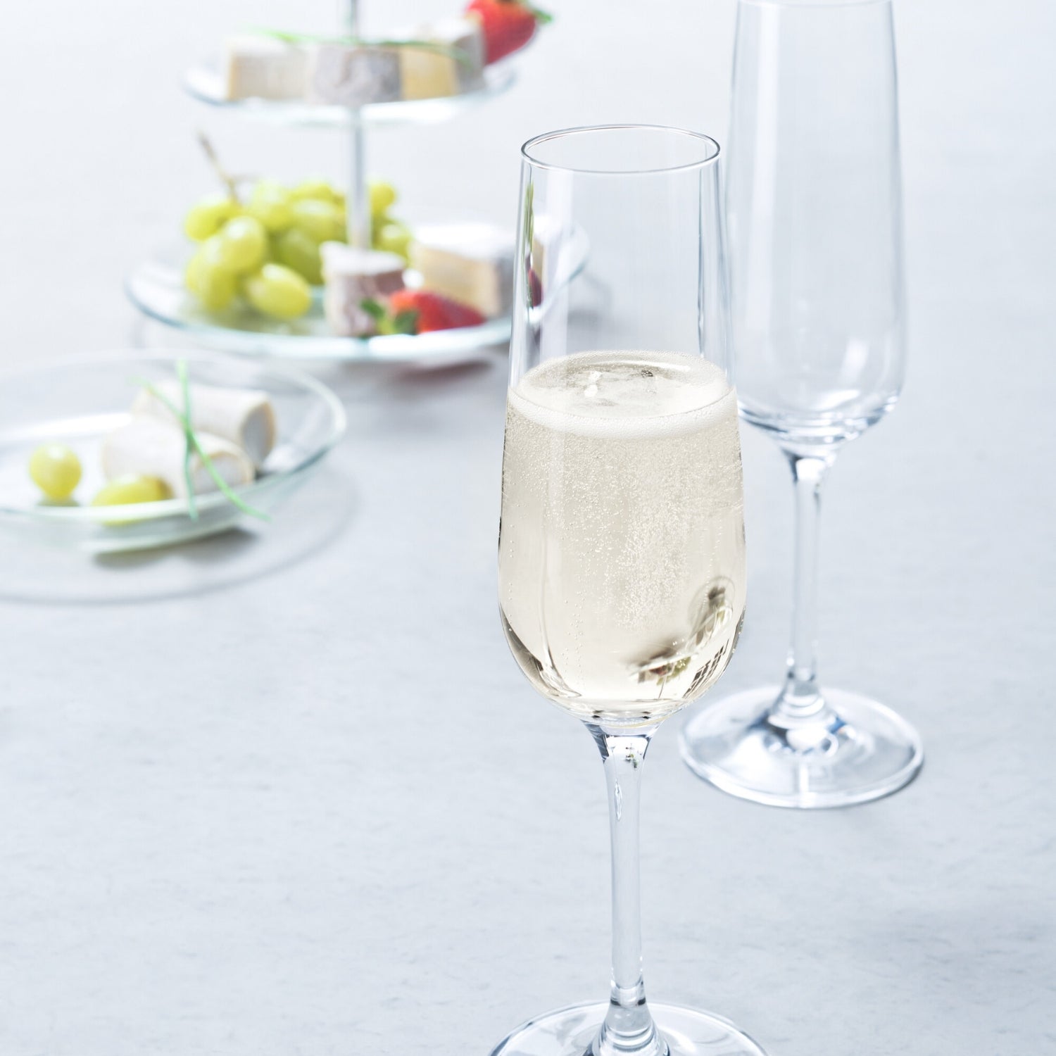 Sektglas TIVOLI mit Champagner gefüllt auf gedecktem Tisch mit Obst und Käse