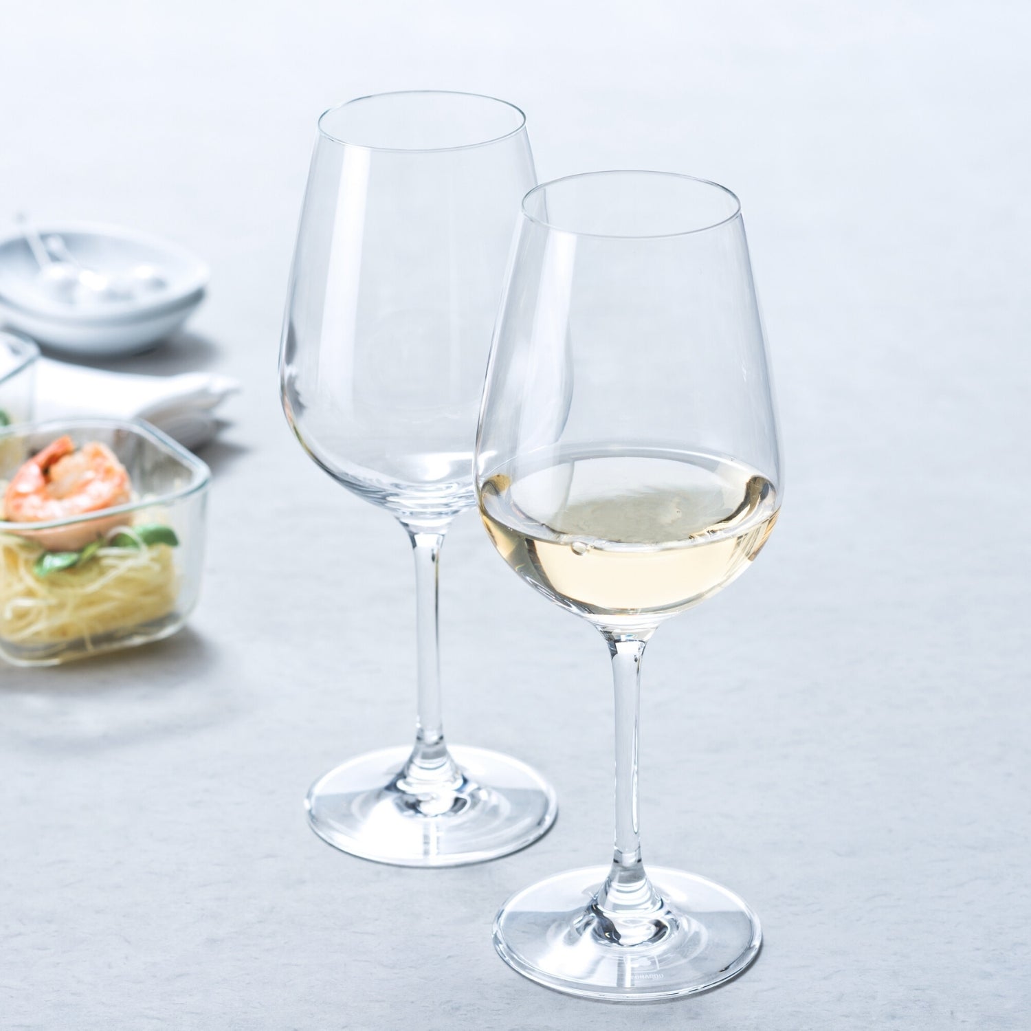 Zwei Weißweingläser TIVOLI, eines leer und eines mit Weißwein gefüllt, auf gedecktem Tisch