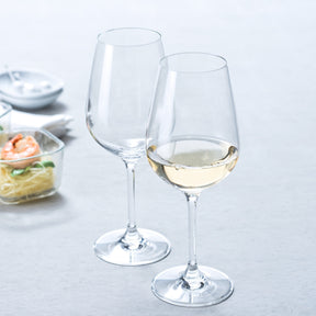 Zwei Weißweingläser TIVOLI, eines leer und eines mit Weißwein gefüllt, auf gedecktem Tisch