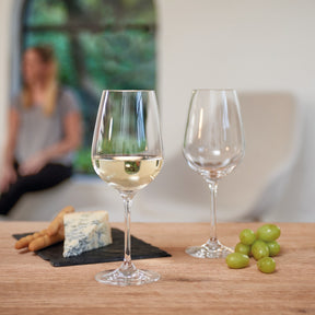 Weißweinglas TIVOLI mit Weißwein, daneben leeres Glas, Käse, Stangen und Trauben auf Holztisch