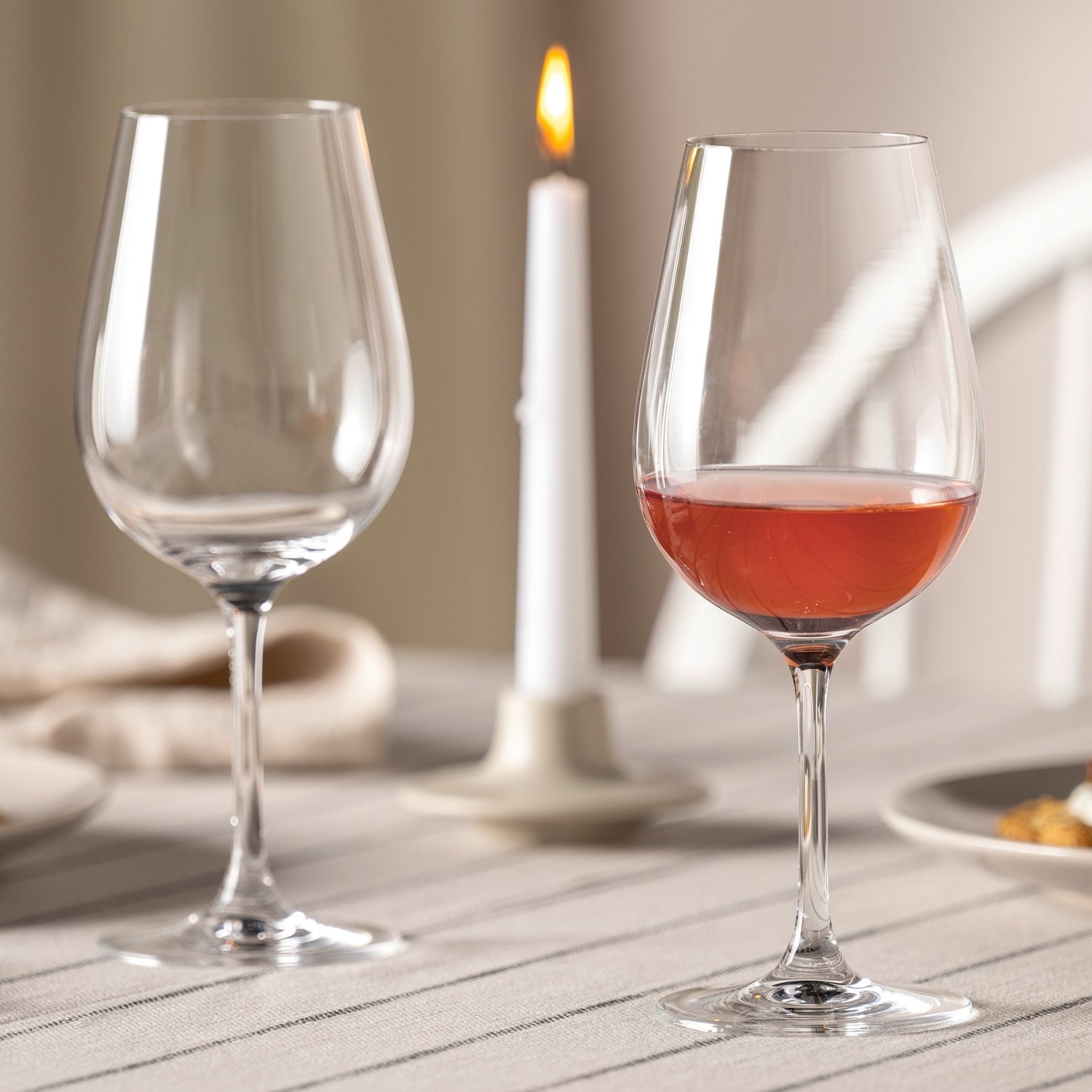 Rotweinglas TIVOLI mit Rotwein gefüllt, leeres Glas daneben, gedeckter Tisch mit Kerze