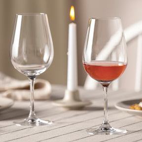 Rotweinglas TIVOLI mit Rotwein gefüllt, leeres Glas daneben, gedeckter Tisch mit Kerze