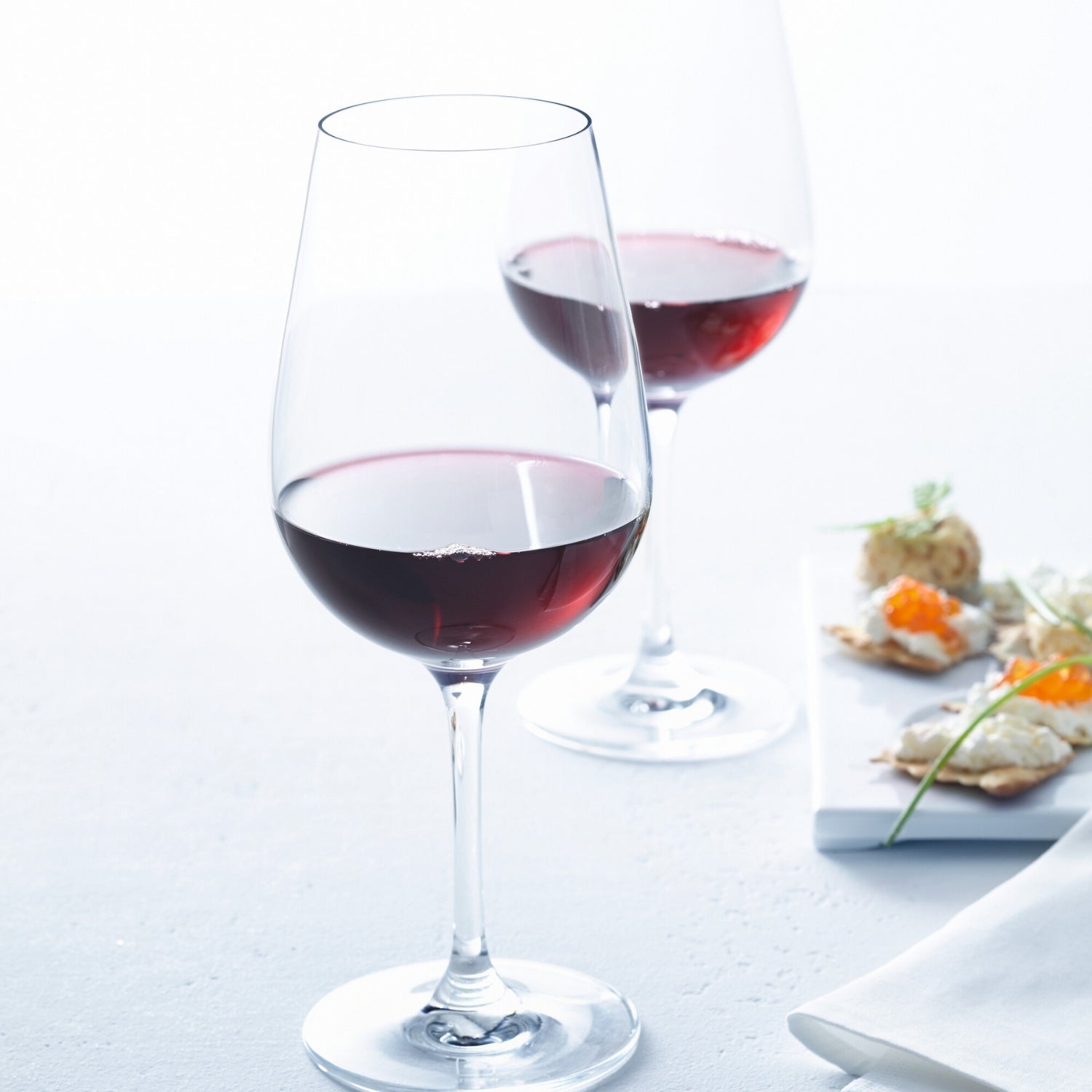 Rotweinglas TIVOLI mit Rotwein gefüllt, Tischgedeck mit Appetithäppchen im Hintergrund