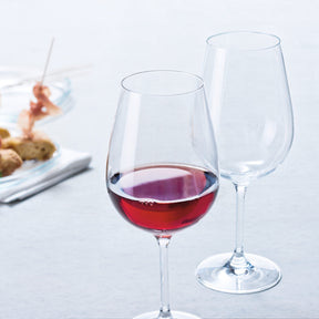 Rotweinglas TIVOLI mit Rotwein gefüllt, daneben leeres Glas, im Hintergrund gedeckter Tisch