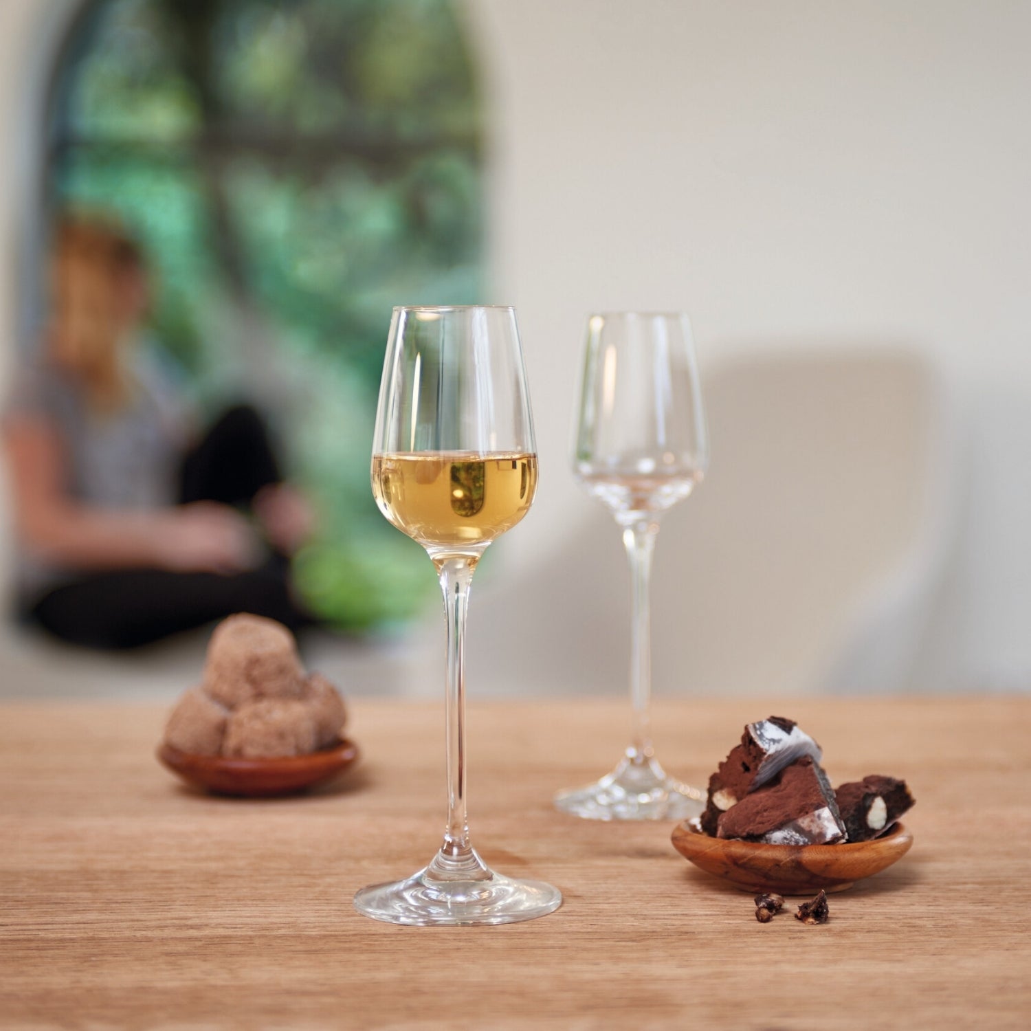 Digestifglas TIVOLI mit Weißwein gefüllt auf Holztisch, daneben leere Gläser und Schokoladengebäck